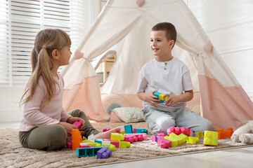 Little kids playing with building blocks near toy wigwam at home © New Africa