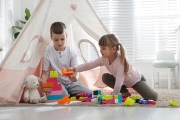 Little kids playing with building blocks near toy wigwam at home © New Africa