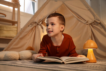 Little boy reading book near toy wigwam at home © New Africa