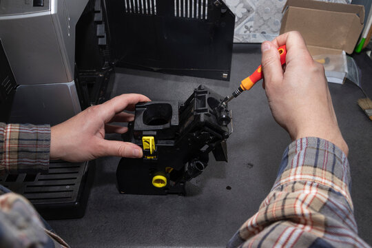 Male hand unscrewing coffee machine brew unit using screwdriver for repair. Concept of coffee machine maintenance, repair, appliance servicing, technical work.