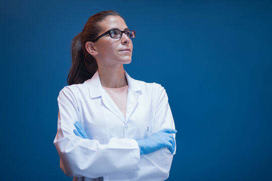 Confident female doctor in lab coat and gloves looking up in clinical blood testing laboratory