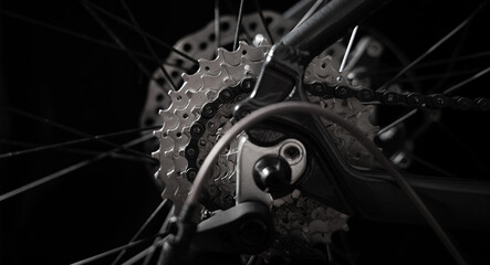 Fototapeta premium Close-up of bicycle rear cassette and chain with visible spokes on black background. Concept of cycling, sport, mechanical engineering, maintenance, repair and performance.