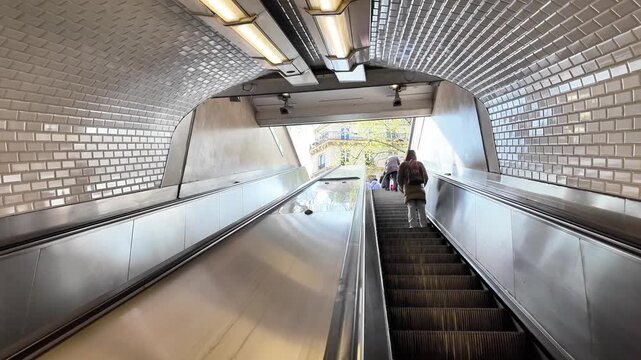Low angle static shot of an escalator rising from a Paris M&eacute;tro station toward the street under a cloudy sky.