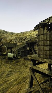 An old western town with wooden buildings. A water tower stands tall in the foreground. The ground is dry and dusty, with hills in the background.