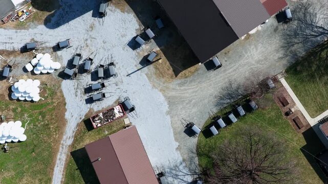 Top down aerial view of Amish farm in Pennsylvania, USA, horse drawn buggies parked near barns and silos, rural countryside setting with traditional lifestyle and agricultural surroundings.