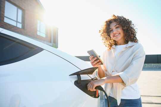 Woman charging electric car at home using mobile phone app