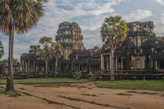 Stone gopura gateway of a Khmer temple with a tall palm tree and sandy path in bright daylight at Angkor, Cambodia.