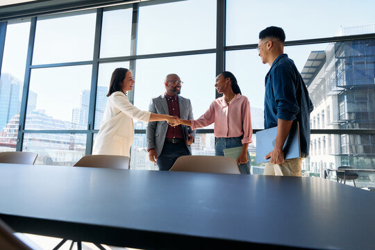 Happy female colleagues shaking hands near team in boardroom at office during daytime