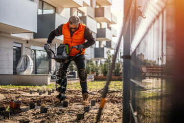Gardener using tools hand-held soil hole drilling machine or portable manual cordless earth auger for prepare the soil for planting plants. © Peter