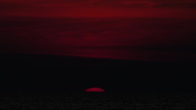 Golden sunset over the sea, captured from a scenic viewpoint. The sun slowly dips below the horizon, casting warm orange and yellow tones. Peaceful and serene atmosphere