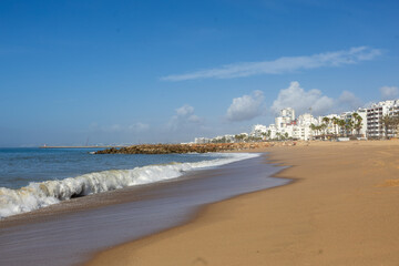 Obraz premium Sandy beach with ocean waves and Faro city Algarve Portugal coastline
