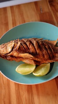 Whole Fried Fish Mojarra Served With Lime Wedges On Blue Plate.