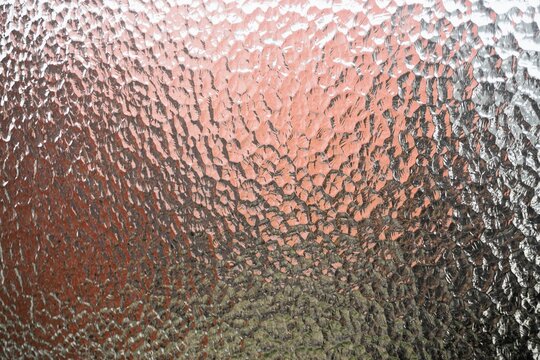 Abstraktes Motiv mit Glasmusterwand vor rot-grau-pinkem Hintergrund mit Licht 