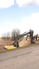 Rząd nowoczesnych koparek gąsienicowych stoi na placu budowy. Potężne, żółte maszyny z długimi ramionami są gotowe do robót ziemnych. W tle widać drzewa i błękitne niebo z delikatnymi chmurami © tomo81