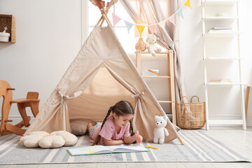 Little girl drawing in sketchbook near toy wigwam at home, space for text © New Africa
