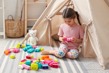 Little girl playing with building blocks near toy wigwam in playroom © New Africa