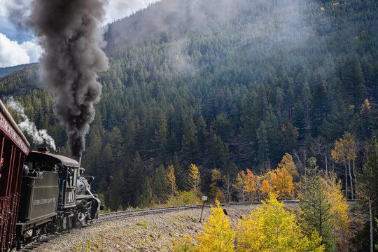 Exhaust smoke rises as the old train goes around the mountain bend