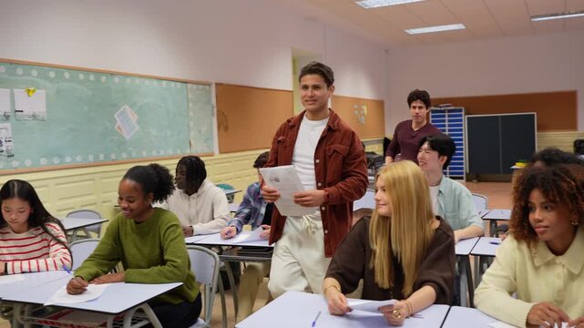 Diverse group of teenage students finishing their tests in a high school classroom and handing them to the female professor one by one