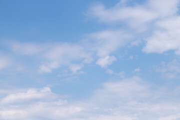 Fototapeta premium A soft, clear blue sky dotted with scattered white clouds and gentle sunlight, ideal for backgrounds, nature themes, relaxation, weather concepts and minimalist design projects.