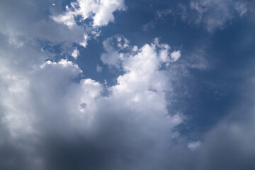 Fototapeta premium Dramatic cumulus clouds gather over a deep blue sky, contrasting bright white tops and dark storm shadows, suggesting changing weather, moodiness, and the power of nature.