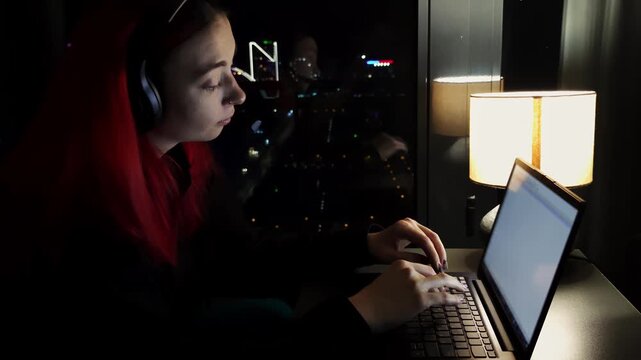 Woman specializing in examining spreadsheets is working under lamp light with city view outside. Caucasian lady reviews reports and tries to finish job before deadline focused on numbers and planning