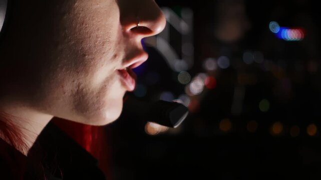 Focused female operator manages crisis communication filmed in closeup. Mouth is speaking into mic in dark room. Support operator is handling critical call with steady breath and clear diction