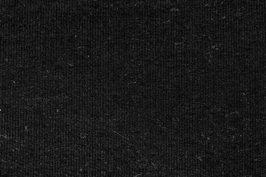 Close-up view of black ribbed fabric with visible textile texture and fine lint details. Dark cloth background with soft woven pattern, suitable for fashion, apparel, textile design, upholstery