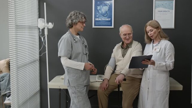 Medium long shot of female Caucasian doctor giving recommendations for hypertension prevention to senior Caucasian man during health check up after nurse measured his blood pressure