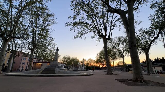 Square with stone fountain and trees at sunset in Perpignan