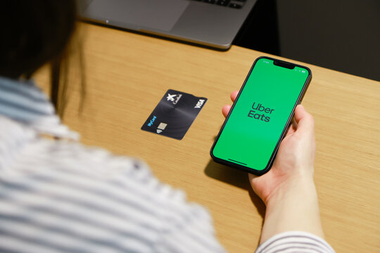 Pamplona, ​​Spain - April 12, 2026. A person holds a smartphone with the Uber Eats app open on the screen. On the table are a bank card and a laptop, suggesting an environment of online food ordering 