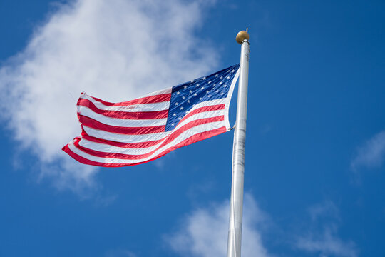 American flag waving on flagpole against blue sky with clouds