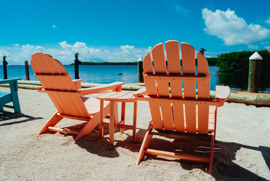 Orange Adirondack chairs on sandy waterfront under blue sky