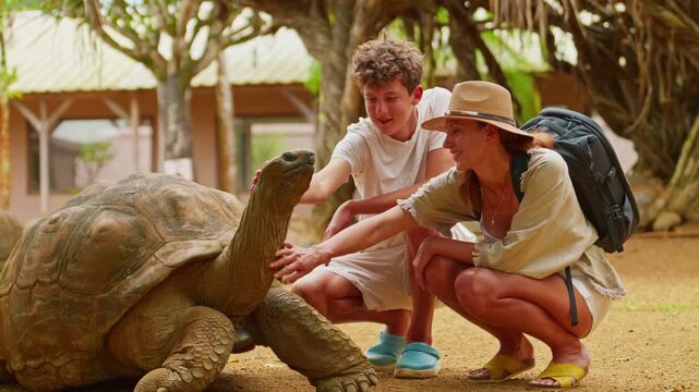 A mother and son pet the head of a rare, giant turtle on the tropical island of Mauritius