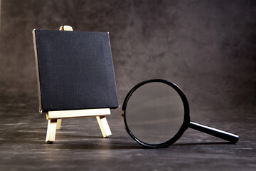 Small black easel with a magnifying glass on a gray background © Artvibe