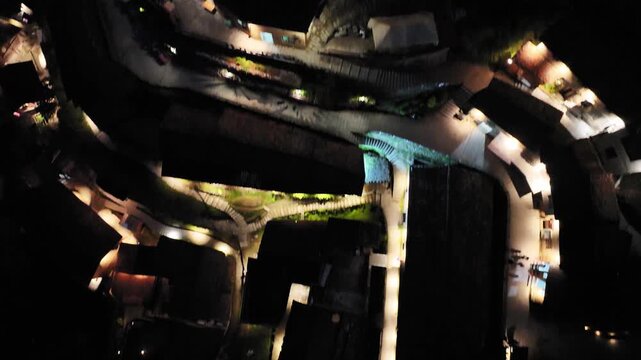 Nighttime aerial view of an ancient village with winding illuminated streets and traditional architecture