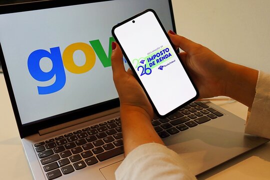 Salvador, Brazil - April 13, 2026: Woman's hand holding a smartphone with Imposto de Renda Receita Federal 2026 logo (Brazil Income Tax Declaration 2026) and gov.br logo in the background. 