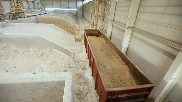 Unloading of open wagons and storage of bulk materials in a industrial warehouse. The interior of a factory clay and sand warehouse. Unloading wagons of clay at the warehouse. Bulk cargo. Unloading