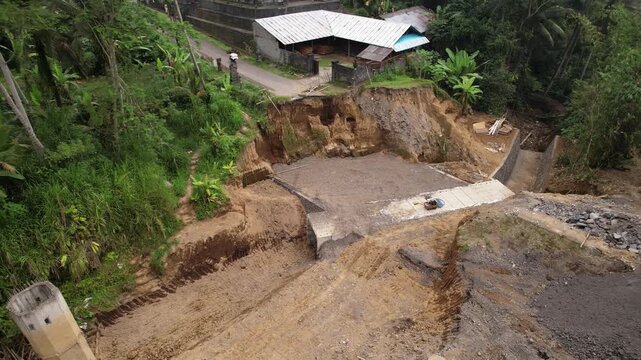 Visible progress in restoring road washed out by river: concrete culvert-pipe for water flow at bottom of ravine is completed, and slope reinforcement has begun. Camera flies up and back