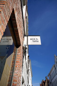 Sch&ouml;ne sanierte alte Fassaden aus braunem Backstein mit Gesch&auml;ft des Optiker ace & tate vor blauem Himmel im Sonnenschein am 08.04.2026 in den Gassen der Altstadt von Br&uuml;gge in Westflandern in Belgien