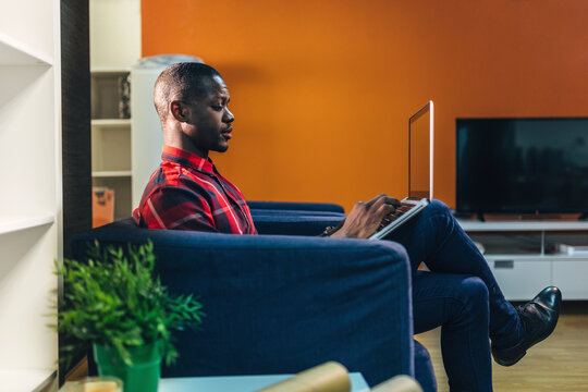 Black Man working on laptop from sofa in modern living room