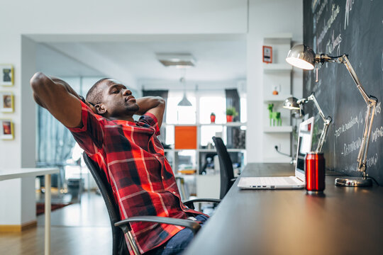 Relaxed black man taking a break at modern office desk