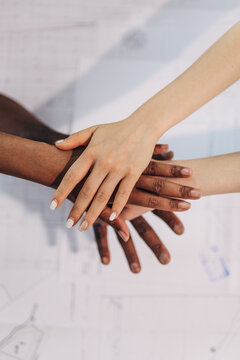Diverse hands stacked in teamwork unity over blueprint