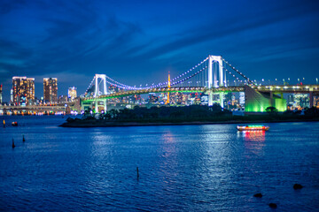 Fototapeta premium Illuminated Rainbow Bridge at night in Odaiba, showcasing Tokyo’s iconic architecture and colorful urban skyline