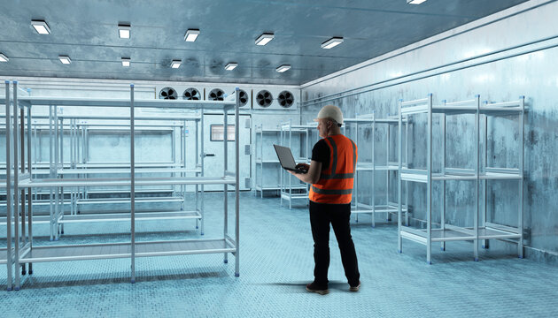 Cold storage inspection, Refrigeration facility. Engineer checks empty freezing warehouse and monitors cooling system performance using laptop.