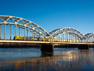 Fototapeta premium A yellow train crosses an arched bridge over the river