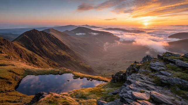 Stunning orange-yellow sunrise from Sharp Edge on Blencathra in Lake District, with reflections in a mountain tarn and a cloud inversion rolling over distant peaks.