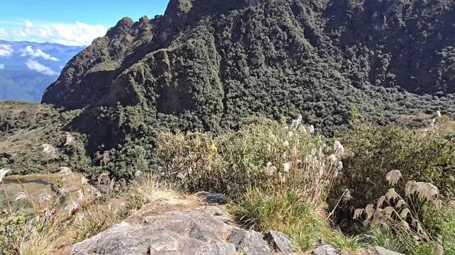 Cusco Region, Peru - 26 June 2024. Inca Trail path winding through high Andes valley, with dry grass, shrubs, steep cliffs, and layered mountains fading into the distance beneath scattered clouds.
