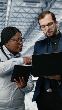 Vertical video Woman optimizes microchip smart factory workflow with coworker, using EDA software. Teamworking colleagues using simulation tool tracking semiconductor production circuit layout defects