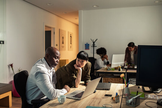 Diverse coworkers collaborating on laptop in open plan office