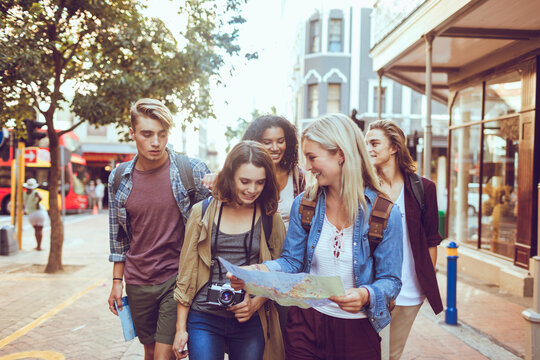 Group of young friends reading a map while walking on city street